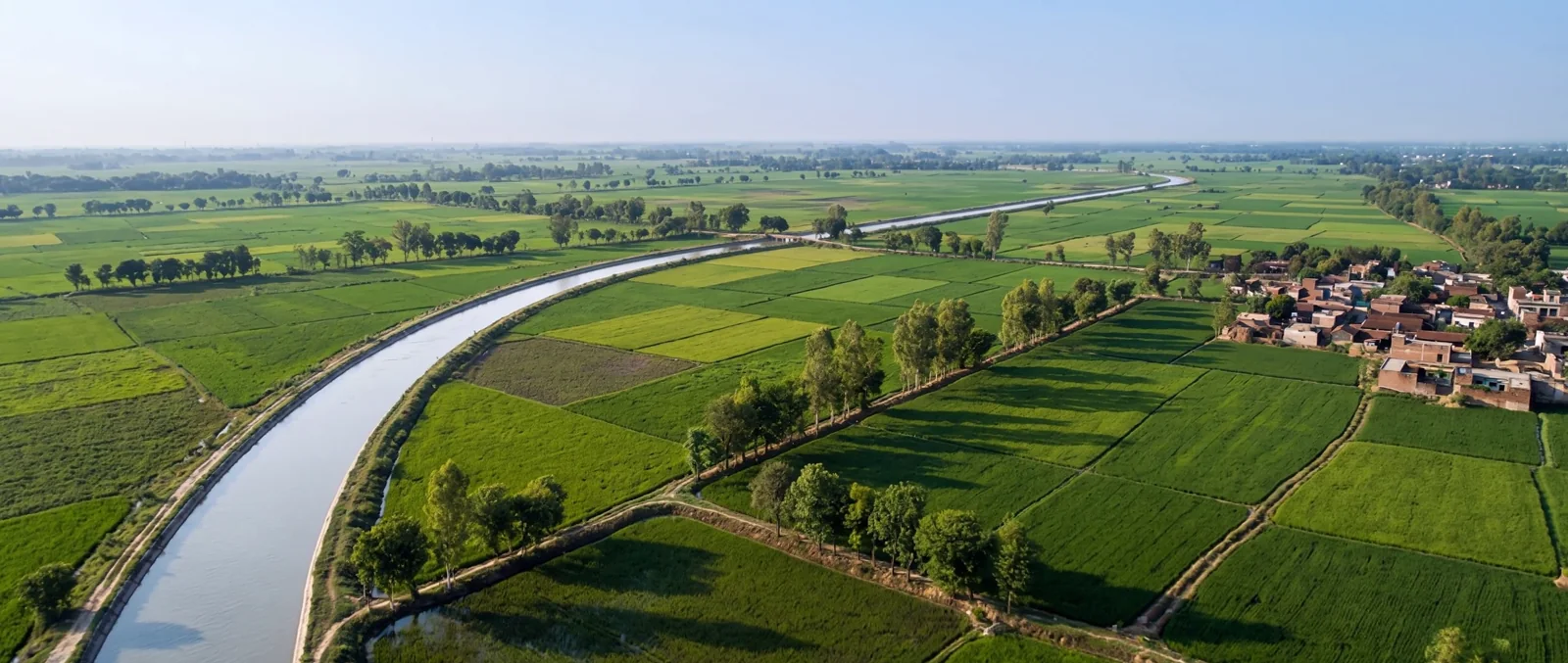 Aerial view of a canal running through green fields beside a brick village